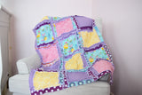 Baby girl crib-size rag quilt and bedding set in purple, pink, yellow, and mint green. Features a soft, patchwork design perfect for a girl&#39;s nursery. This cozy quilt is a quick-ship item, ideal for adding comfort and color to a baby crib
